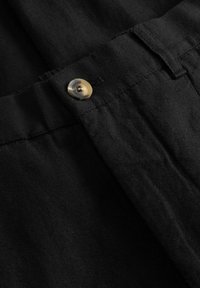 Pojas crnih platnenih hlača s jednim smeđe-bež gumbom provučenim kroz rupicu za gumb.