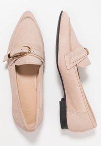 Beige suède loafers met een spitse neus, een gouden gespaccent en een vlakke zwarte zool. Glad textuur met gestikte details.