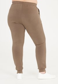 Bruna sweatpants med elastisk midjeband och mudd, slät textur, åtsittande design, ihop med vita sneakers.