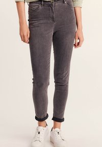 Jeans skinny in denim grigio con vita media, cinque tasche e orli arrotolati, abbinati a sneakers bianche. La texture appare liscia.