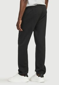 Sorte sweatpants med elastisk talje, tapered ankler og glat stof. Båret med hvide sneakers med sorte accenter.