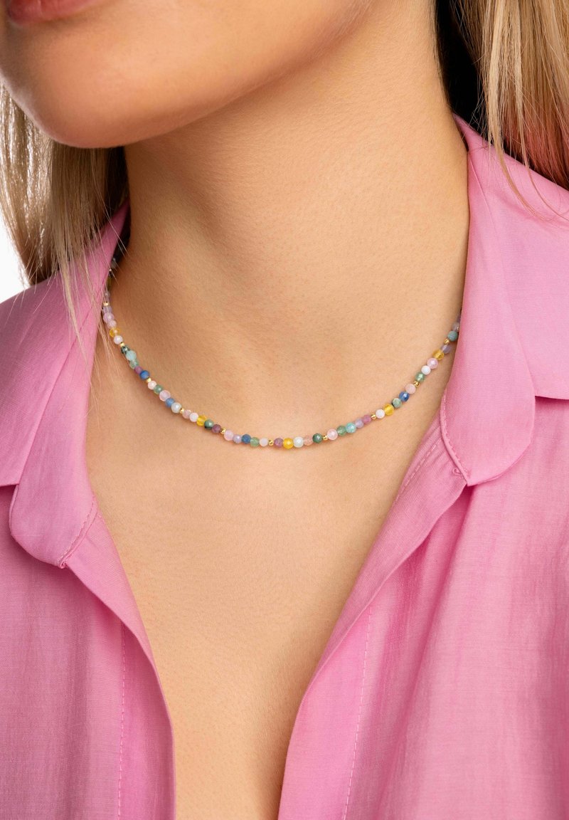 Femme portant un collier multicolore en perles et une chemise rose à col, montrant son cou et le bas de son visage.