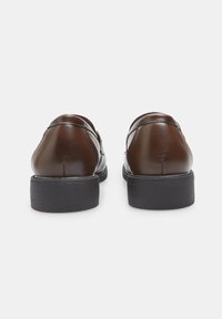 Chaussures en cuir marron au fini lisse, avec des talons ronds et de subtils détails de couture à l'arrière. La semelle est noire avec une légère texture.