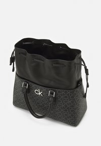 Černá taška typu tote s texturovaným tkaným tělem s opakujícím se vzorem loga. Hladká horní část s tažným uzávěrem na šňůrku. Stříbrné kovové doplňky.