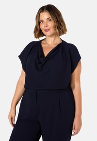 Marinblus med mössa och korta ärmar, tillverkad av mjukt tyg, med avslappnad passform och draperad design, i kombination med skräddarsydda byxor.