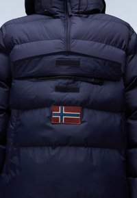 Giubbotto piumino blu navy con tasca con zip, dettagli in velcro e una toppa orizzontale con la bandiera norvegese sul davanti. Materiale testurizzato e isolato.