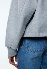 Grijze fleece sweatshirt met een ribbelmanchet, gecombineerd met blauwe denim jeans. De stof heeft een zachte textuur en de pasvorm lijkt ontspannen.