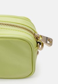 Borsa cosmetica in nylon verde con hardware dorato, dotata di doppia cerniera e charm con logo al tirante della cerniera, forma quadrata, texture liscia.