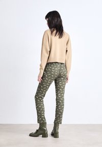 Beige gebreide trui met geribbelde zoom en manchetten, gecombineerd met groene dierenprintbroeken. Zwarte enkellaarsjes met een chunky hak en een gladde textuur.