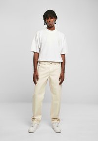 Jean clair, coupe décontractée, associé à un t-shirt blanc surdimensionné. Le mannequin porte des baskets blanches. Design simple, matériel minimal.