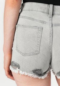Grå denimshorts med frynser i kanten, slitt detaljer og en enkelt baklomme. Fitted design med høy midje. Glatt tekstur.