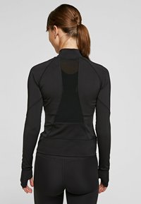 Chaqueta deportiva negra de manga larga, con cuello alto y un panel de malla en la espalda. Cuenta con agujeros para los pulgares y un diseño elegante para el rendimiento.