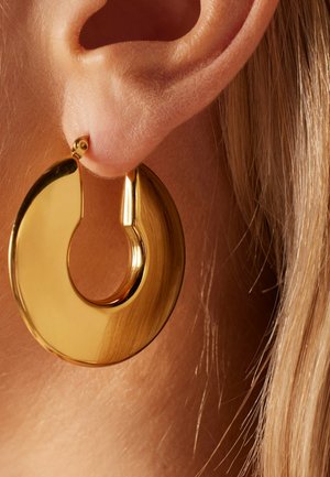Gold circular hoop earring with a polished finish, featuring a smooth texture and a unique cut-out design, attached to an ear.