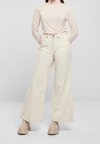 Helle, weite Hose in Cremefarbe mit hoher Taille, fünf Taschen und dezenten Nähten, kombiniert mit einem hellrosa, langärmeligen Rollkragenpullover.