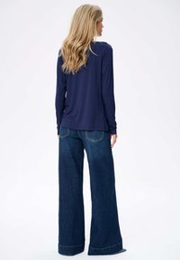 Navyblauer Langarmoberteil mit lockerer Passform, kombiniert mit weit geschnittenen blauen Jeans. Die Jeans besitzen Gesäßtaschen und umgeschlagene Säume.