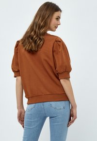 Brun puffärmad tröja med rund krage och ribbad nederkant, i kombination med ljusblå skinny jeans. Slätt bomullstyg och avslappnad passform.