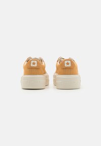 Oranssi kangassneakerit, joissa on valkoinen kumipohja, ja joissa on tähti-logo kannassa sekä hienovaraiset tekstuurit yläosassa.