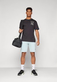 Must lühikeste varrukatega T-särk valge logoga, helesinised lühikesed püksid, mustad spordijalatsid ning musta tekstuuriga jõusaalikott käes.