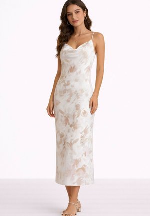 Femme portant une robe midi blanche sans manches avec un motif floral beige, des bretelles fines et des sandales à talons beiges, debout devant un fond uni.