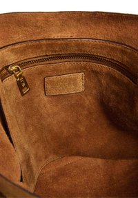 Interno di una borsa a tracolla in suede marrone con una tasca con zip dorata e un vano laterale cucito. Tessuto morbido e strutturato con un design semplice.