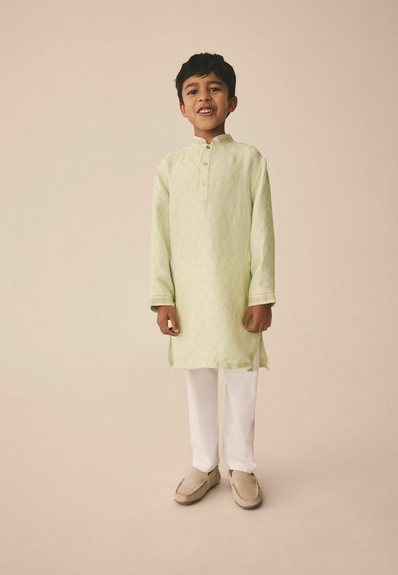 Helles grünes Kurta mit Diamantmuster, geknöpftem Ausschnitt und langen Ärmeln, kombiniert mit weißen Hosen und beigen Slippern.