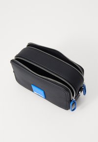 Pungă multifuncțională neagră, realizată din material texturat, dotată cu două fermoare, accente din metal albastru și un patch rectangular cu logo albastru.