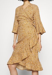 Vestido estampado floral en amarillo mostaza con mangas de campana de tres cuartos, dobladillo volante y una tela ligera y texturizada.