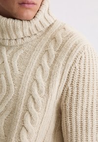 Beżowy sweter z golfem wykonany z grubego splotu. Posiada teksturowane wzory oraz miękką, grubą wełnianą mieszankę.