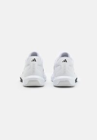 Zapatillas deportivas blancas con parte superior de malla, collar acolchado, suelas de goma y etiqueta "TRAINING" en el talón. Acentos negros cerca de la suela.