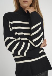 Schwarz-weißer gestreifter Rollkragenpullover mit lockerer Passform, breiten Ärmeln und geripptem Textur, der das auffällige Streifenmuster betont.