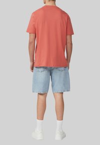 T-shirt en coton rouge à coupe décontractée, associé à un short en denim bleu clair. Des baskets blanches et des chaussettes blanches de longueur mi-mollet complètent le look.