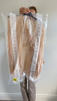Blote blouse met gerimpelde voorkant. Verpakt in helder plastic met een zwarte hanger, voorzien van witte straps met de tekst "S." Hangende prijslabel zichtbaar.