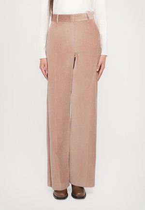 Pantalons en velours côtelé beige clair à pattes larges avec des rayures verticales, taille haute et passants de ceinture, associés à des chaussures marron.