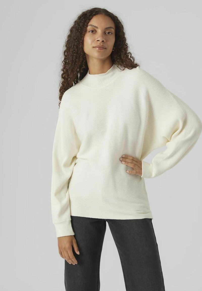 Weißer gerippter Pullover mit hohem Kragen, lockerer Passform und langen Ärmeln, kombiniert mit dunklen Jeans. Glatte Textur; minimalistisches Design.