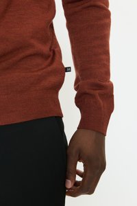 Hosszú ujjú, rozsdabarna színű pulóver puha kötött anyagból, bordázott mandzsettával és szegéllyel. Oldalán kis címkével.
