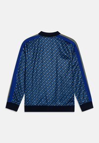 Niebieska kurtka w wzory wykonana z gładkiej tkaniny, z geometrycznymi kształtami, kontrastującymi granatowymi i szarymi paskami na rękawach oraz prążkowanymi mankietami.