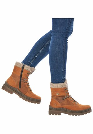 Bottines en suédine marron avec un revers en fourrure, un design à lacets et une fermeture éclair sur le côté. Elles présentent une semelle texturée pour une meilleure adhérence et une bordure marron contrastante.