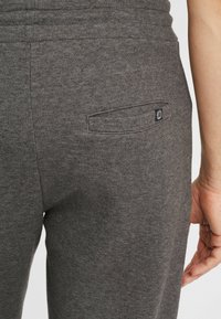 Sivé joggerové nohavice vyrobené z pleteného materiálu, s bočnou zadnou vreckom a malou nášivkou značky pri vrecku. Hladký povrch a zúžený strih.