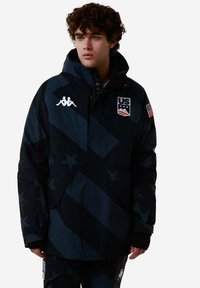 Giacca nera e blu scuro con motivi a stella, cappuccio, dettagli con logo e chiusura lampo frontale. Include toppe con bandiera statunitense e logo del marchio.