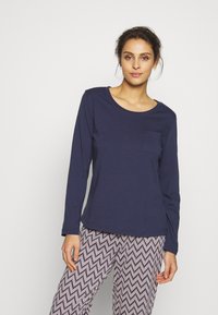 Chemise à manches longues bleu marine avec un col rond et une poche avant, assortie à un pantalon à motifs avec un design en zigzag en noir et blanc.