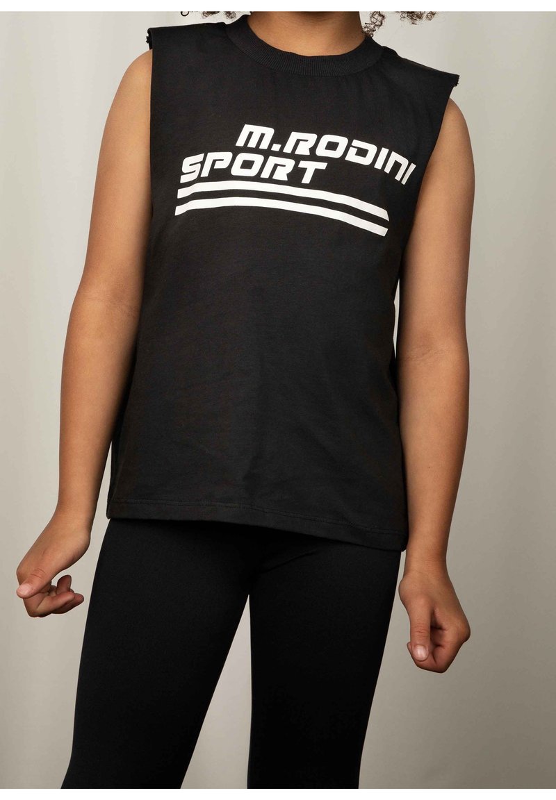 Personne portant un débardeur noir avec le texte blanc "M.RODINI SPORT" et des leggings noirs assortis sur un fond uni.