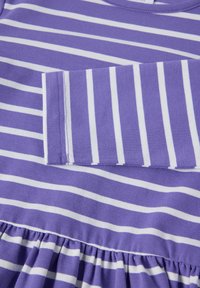 Violetti ja valkoinen raidallinen pitkähihainen paita, jossa on kerätty kangas yksityiskohtana alareunassa.