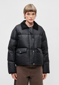 Črna napihljiva jakna z rebrastim črnim ovratnikom, dvema sprednjima žepoma in zapiranjem na gumbke; prešita zasnova dodaja izolacijo in obliko.