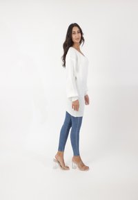 Witte gebreide trui met een V-hals, lange pofmouwen, gecombineerd met blauwe skinny jeans en transparante blokhak sandalen.