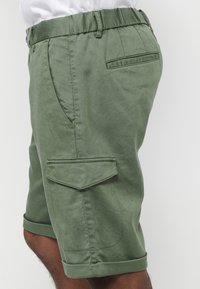Grüne Cargo-Shorts mit flachem Bund, Gürtelschlaufen, Seitentaschen und umgeschlagenen Säumen. Hergestellt aus einem glatten, strapazierfähigen Stoff mit einem dezenten Glanz.