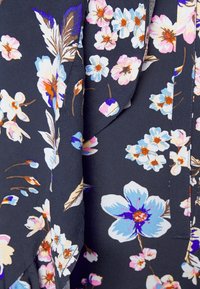 Tissu foncé avec un motif floral de fleurs bleues, roses et blanches et des feuilles marron, présentant des coutures et des plis visibles.