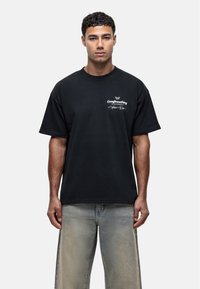 Czarny t-shirt z krótkim rękawem wykonany z bawełny, z białym nadrukiem graficznym i luźnym krojem. W połączeniu z jasnoszarymi zniszczonymi dżinsami.