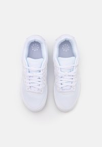 Paire de baskets blanches avec lacets, vues de dessus sur un fond clair uni.