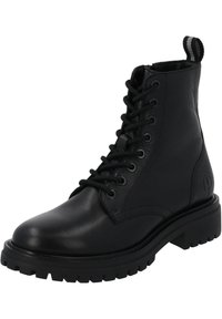 Bota de combate de cuero negro con punta redonda, parte frontal con cordones y suela de goma texturizada. Cuenta con una lengüeta con rayas grises.