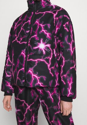 Schwarze Steppjacke und Hose mit leuchtend pinken Blitzmustern und einem Frontreißverschluss, getragen von einer Person mit sichtbaren Händen.